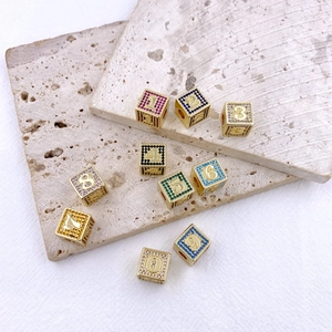 Dettaglio macro di ciondoli a dado placcati oro con zirconi colorati e numeri incisi
