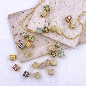 Dettaglio di ciondoli a dado con lettere placcati oro e zirconi colorati su catena snake
