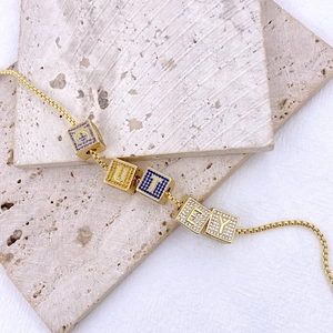 Dettaglio collana dorata con cubi di zirconi colorati e ciondoli con la scritta CUTEY