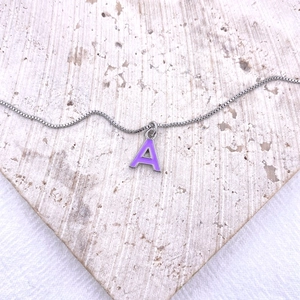 Silver letter A pendant necklace with purple enamel on a modern textured stone display