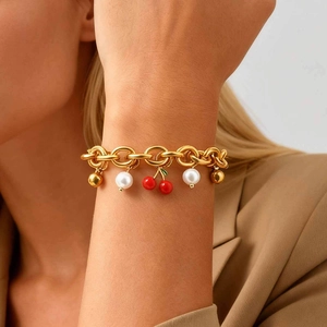 Dettaglio del bracciale a catena dorata con ciliegie rosse e perle bianche sul polso