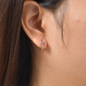 Eleganti orecchini a cerchio dorati con fiore in zircone viola indossati su un lobo femminile