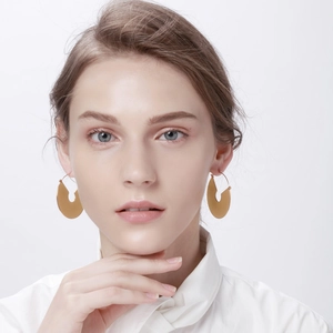 Détail de boucles d'oreilles demi-cercle en or mat portées par un mannequin chic