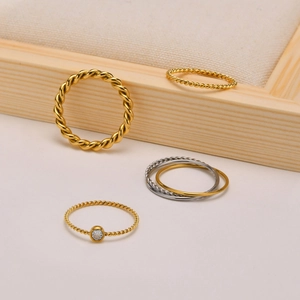 Detalle de cuatro anillos trenzados de oro y plata con circón en soporte de madera