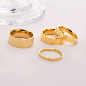 Flat lay of four polished gold stainless steel rings with varying widths on a soft background
