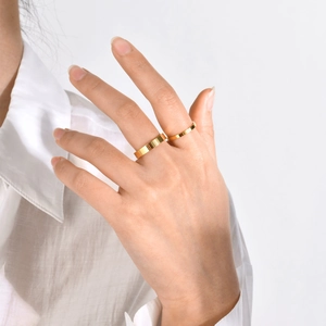 Close-up of minimalist gold-plated stainless steel band rings on a hand with glossy finish