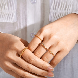 Vista detallada de anillos dorados trenzados apilados y anillos delicados con un diamante