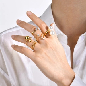 Detalle de cinco anillos de acero dorado con perlas y pedrería en una mano de mujer