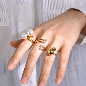Set de tres anillos abiertos dorados con perlas artificiales y circón en mano de modelo