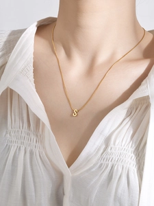 Detalle de un colgante de letra S en oro pulido con una cadena fina en una modelo