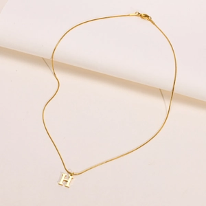 Detalle de collar de cadena de serpiente de acero inoxidable dorado con colgante H