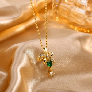 Detalle de collar dorado con corazón verde y colgante de lazo de circón en seda