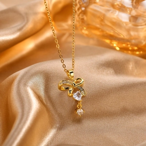 Detalle del collar de lazo dorado con circonita de corazón sobre tela de seda dorada