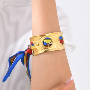 Detail of wide gold cuff bracelet featuring hammered texture and colorful silk scarf knot