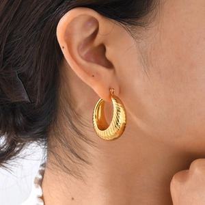 Macro detail of golden croissant hoop earrings with embossed spiral texture on model