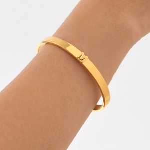 Dettaglio di un bracciale rigido dorato lucido con una lettera M 3D in stile minimal