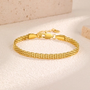 Close-up of golden mesh chain bracelet with lobster clasp on beige stone background