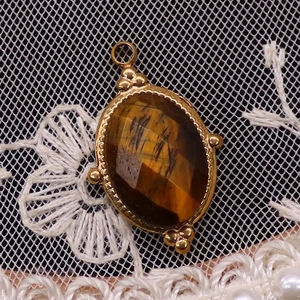 Detail eines ovalen Tigerauge-Anhängers mit goldenem Seilrand und Perlenverzierung