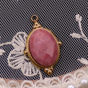 Detail eines ovalen rosa Natursteinanhängers mit vergoldeter Perlenkante aus Edelstahl