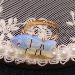 Detalle de anillo de opalo en forma de pez con alambre dorado en fondo de encaje