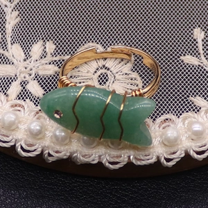 Detalle de anillo en forma de pez con piedra verde y alambre dorado sobre encaje