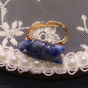 Detalle de anillo artesanal de alambre con gema de pez azul y un pequeño detalle de cristal