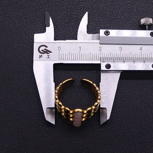 Detail view of gold adjustable ring with pink gemstone being measured by a caliper