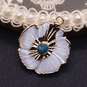 Macro shot of flower pendant with white shell petals and blue stone set in gold frame