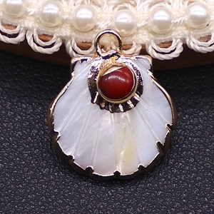 Macro detail of fan-shaped white shell pendant with red gemstone and gold plated edging