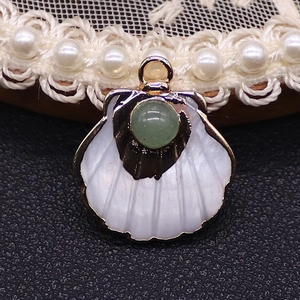 Macro detail of fan-shaped shell pendant with golden metal and green gemstone inlay