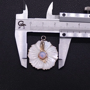 Detail shot of a flower-shaped shell pendant with opal inlay measured by calipers