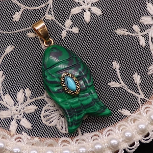Vista macro de colgante de pez de malaquita con incrustación turquesa y detalle dorado