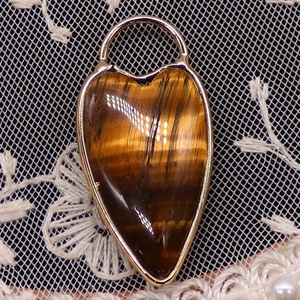 Macro shot of tiger eye heart pendant with gold plated frame on white lace background
