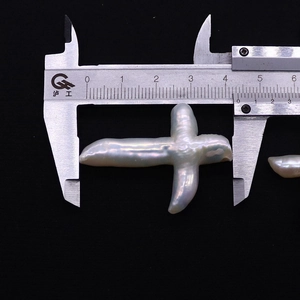 Gros plan d'une grande perle baroque en forme de croix mesurée avec un pied à coulisse