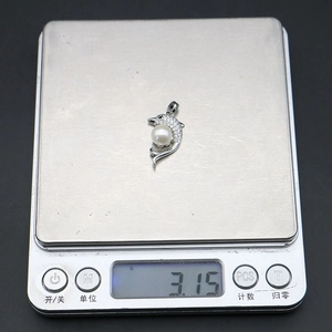 Macro detail van dolfijn hanger met parel en zirkonia op een digitale weegschaal van 3,15g