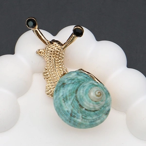 Detailed view of snail brooch with gold texture and turquoise spiral shell on white stand
