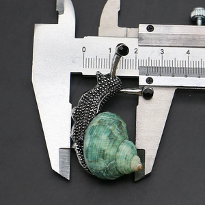 Macro detail of snail brooch with natural green shell and crystal eyes on silver metal