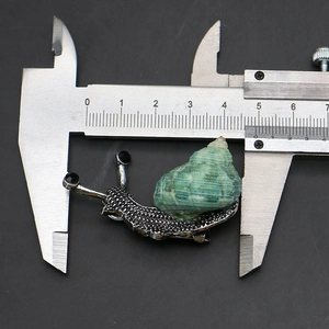 Detail view of snail brooch with green shell and silver texture next to a caliper