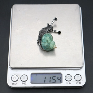 Macro detail of snail-shaped brooch with green shell on silver scale weighing 11.54g