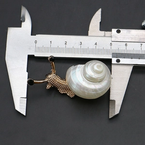 Macro view measuring a gold snail brooch with natural shell inlay using a metal caliper
