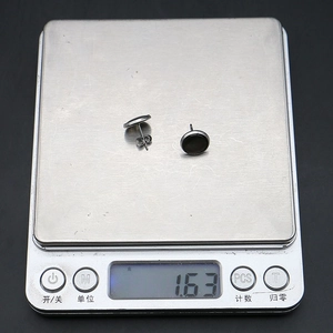 Dettaglio degli orecchini a bottone neri su una bilancia digitale che pesa circa 1,63 g