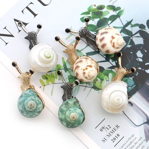 Golden snail brooch set with natural shell and crystal accents on a stylish background