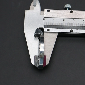 Detailed measurement of the 0.5cm thickness of a round shell pendant using a caliper