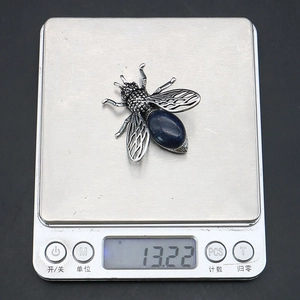 Nahaufnahme einer bienenförmigen Brosche mit einem Gewicht von 13,22 g auf einer Waage