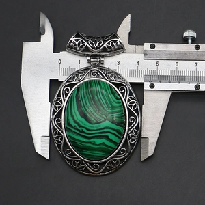 Detailed macro view showing a vintage oval malachite pendant measured with a caliper