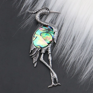 Detailed close-up of crane brooch with silver feather texture and iridescent abalone shell