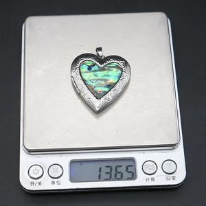 Dettaglio di un medaglione a cuore su una bilancia digitale con un peso di 13,65 grammi