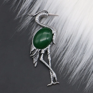 Detailed view of crane brooch with vintage silver plating and green gemstone inlay