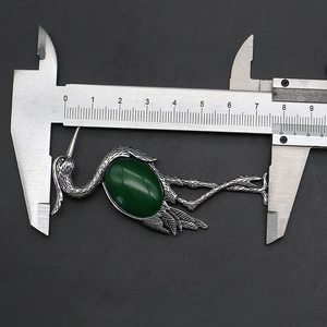 Detailed view of crane brooch measuring 8.3cm with green gemstone and silver feather texture