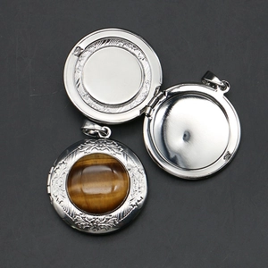 Locket necklace detail featuring round tiger eye stone and carved floral metallic patterns